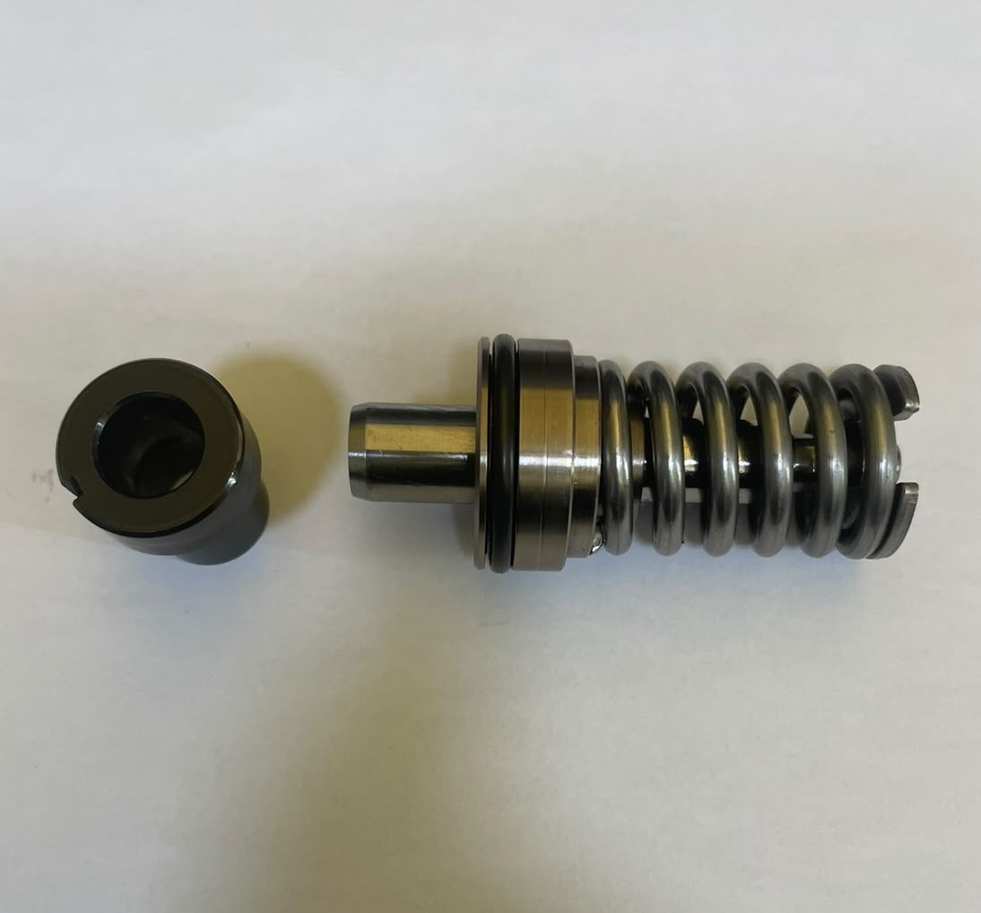 Metal compression damper with a coiled chrome spring and cylindrical plunger, laid beside a round end cap on a white background.